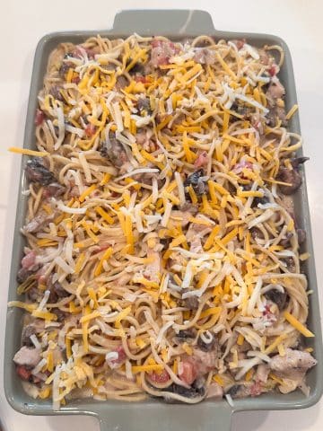 A pan of chicken tetrazzini with shredded cheese on top, before baking.