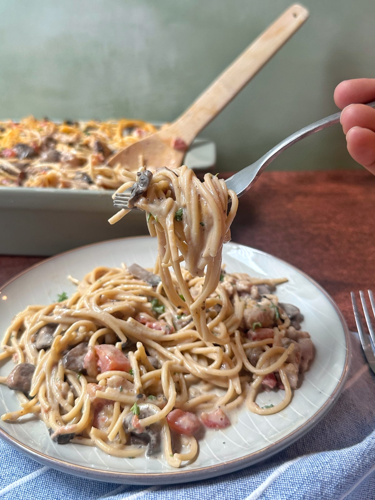 A forkful of chicken spaghetti on a plate with extra helpings in the background.
