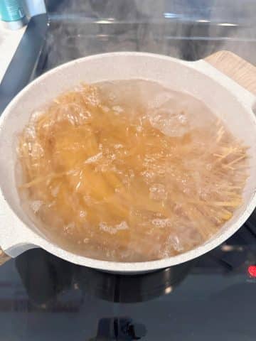 A pot filled with water and spaghetti noodles boiling.