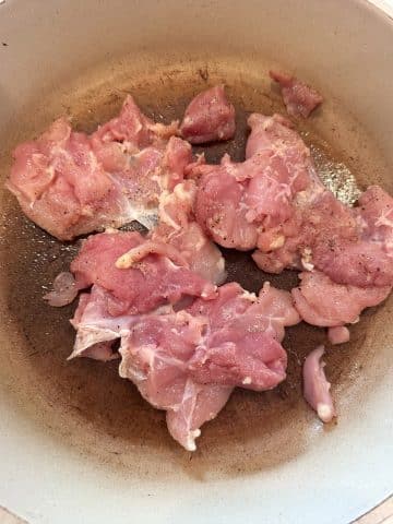 Pieces of seasoned raw chicken thighs cooking in a skillet.