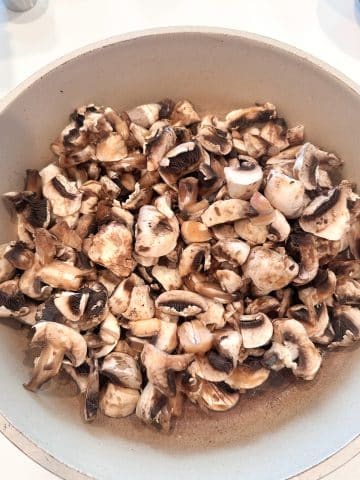 A cream colored skillet filled with chopped mushrooms.