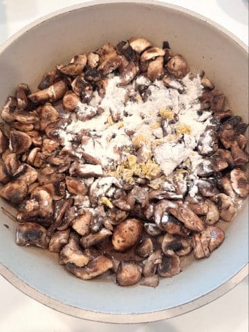 A pan of sautéed mushrooms with flour and seasonings on top.