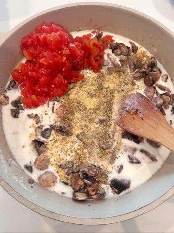 A pan filled with sautéed mushrooms, cream, diced tomatoes, and seasonings.