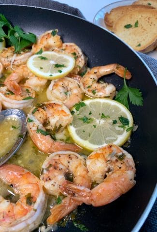 skillet with garlic shrimp scampi, lemon slices, and parsley with bread on the side