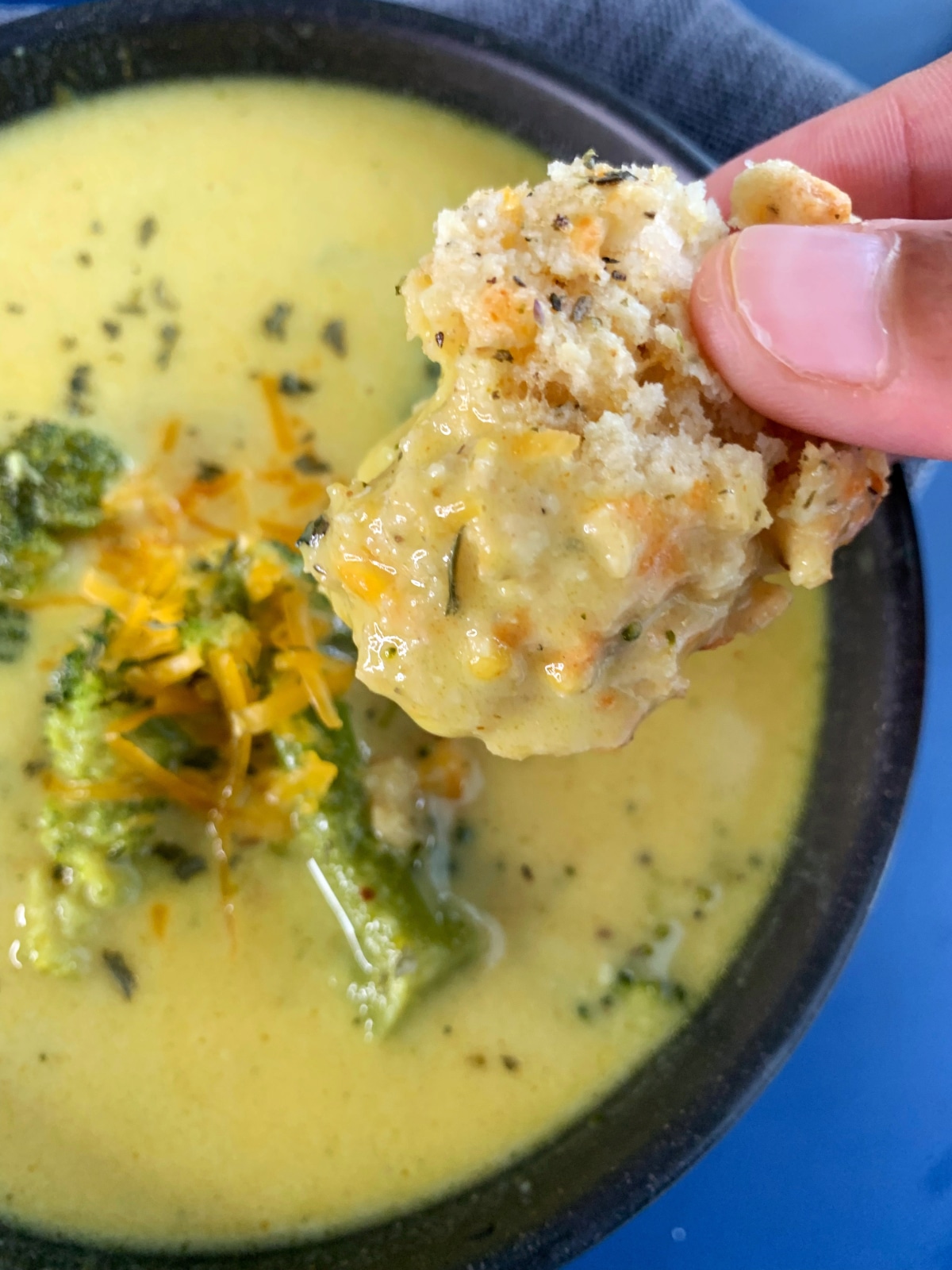 A hand dipping a cheddar drop biscuit into a bowl of broccoli cheddar soup.