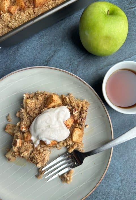 A slice of apple pie baked oats with whipped cream/Greek yogurt on top.