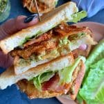 A hand holding two stacks of Fried Green Tomato sandwiches with more sandwich ingredients in the background.