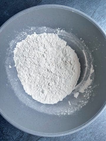 A mixing bowl containing flour, baking powder, baking soda, and salt mixed together.