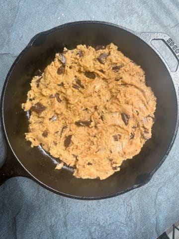 Chocolate chip cookie dough placed into a cast iron skillet.
