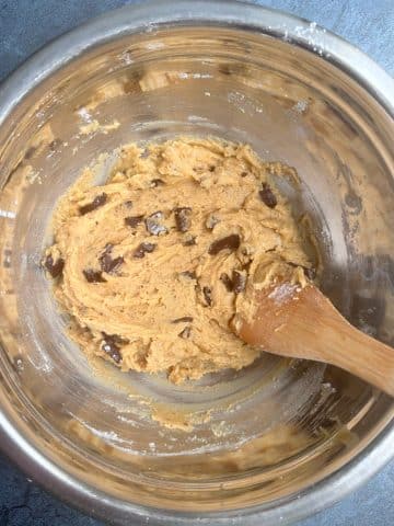 Peanut butter chocolate chip cookie dough with a wooden spoon sticking out of it.