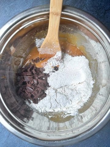 A wooden spoon preparing to mix dry ingredients and chocolate chips into wet ingredients in a bowl.