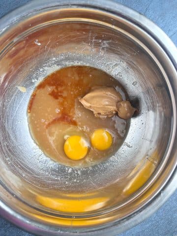 A mixing bowl containing creased sugar, eggs, peanut butter, and vanilla extract.