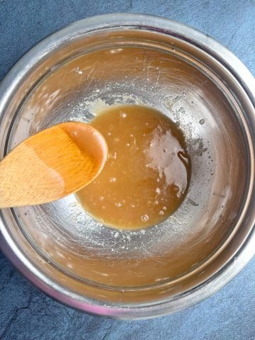Wet ingredients for cookie dough mixed well, dropped into a mixing bowl from a wooden spoon.