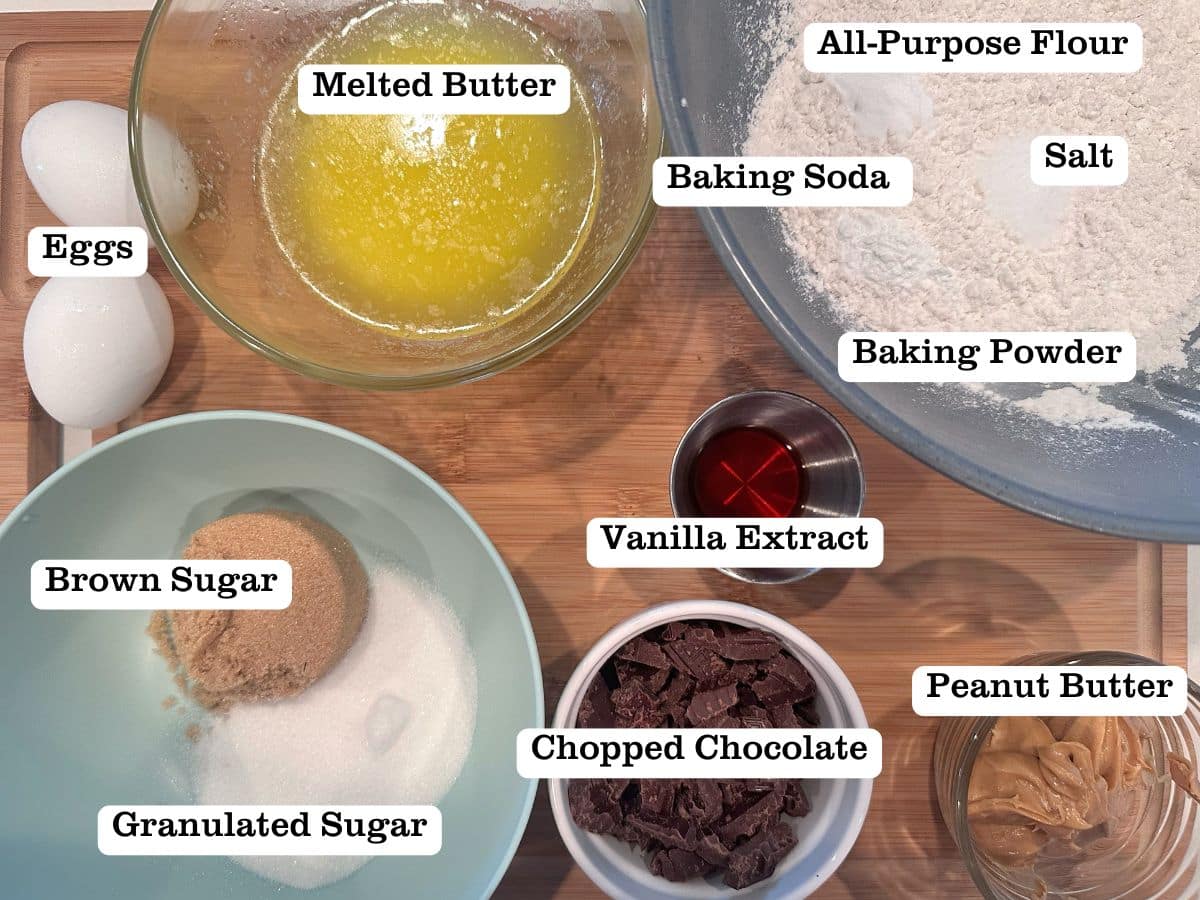 A wooden board containing ingredients for a cookie skillet, including melted butter, brown sugar, chopped chocolate, and peanut butter.