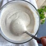 A bowl of homemade ranch with a spoon scooping a portion.