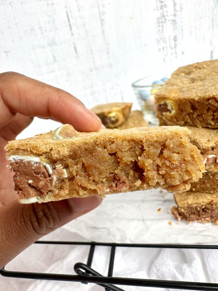 A hand holding a square of Mini Cadbury Egg Blondies with more of the dessert in the background.