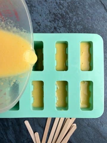 A cup of blended peaches being poured into a silicone popsicle mold.