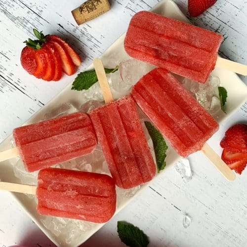 Homemade boozy Strawberry Rosé popsicles on a bed of ice with sliced strawberries on the side.