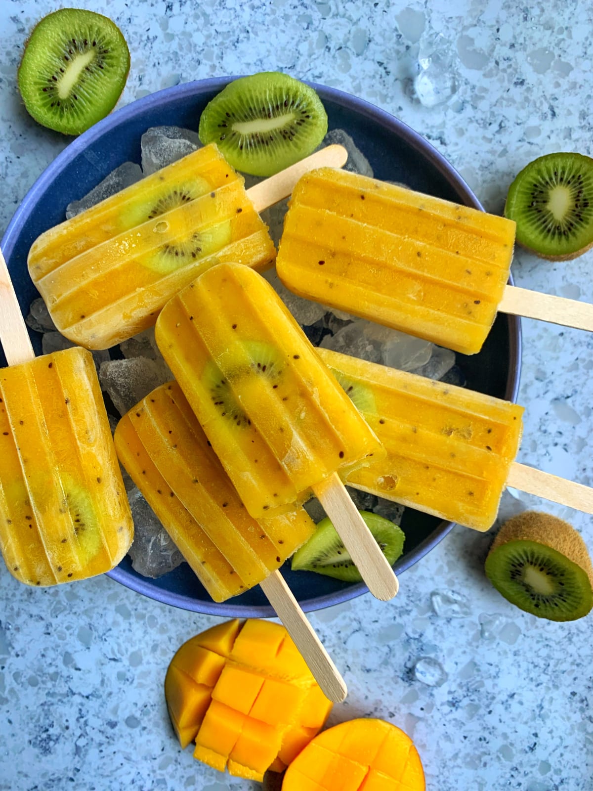 A bowl of homemade mango-kiwi popsicles sitting on ice cubes.