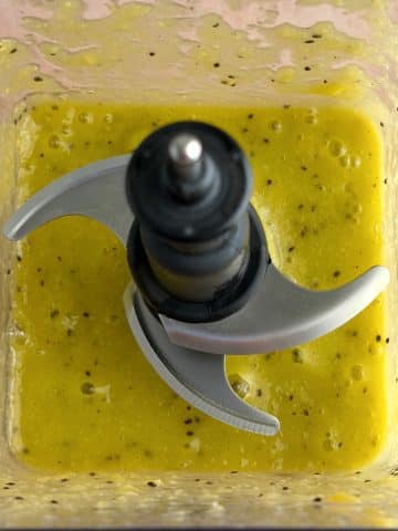 A blender cup filled with blended mangoes and kiwi.