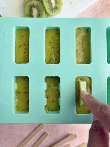A popsicle mold filled with popsicle juice and kiwi slices.