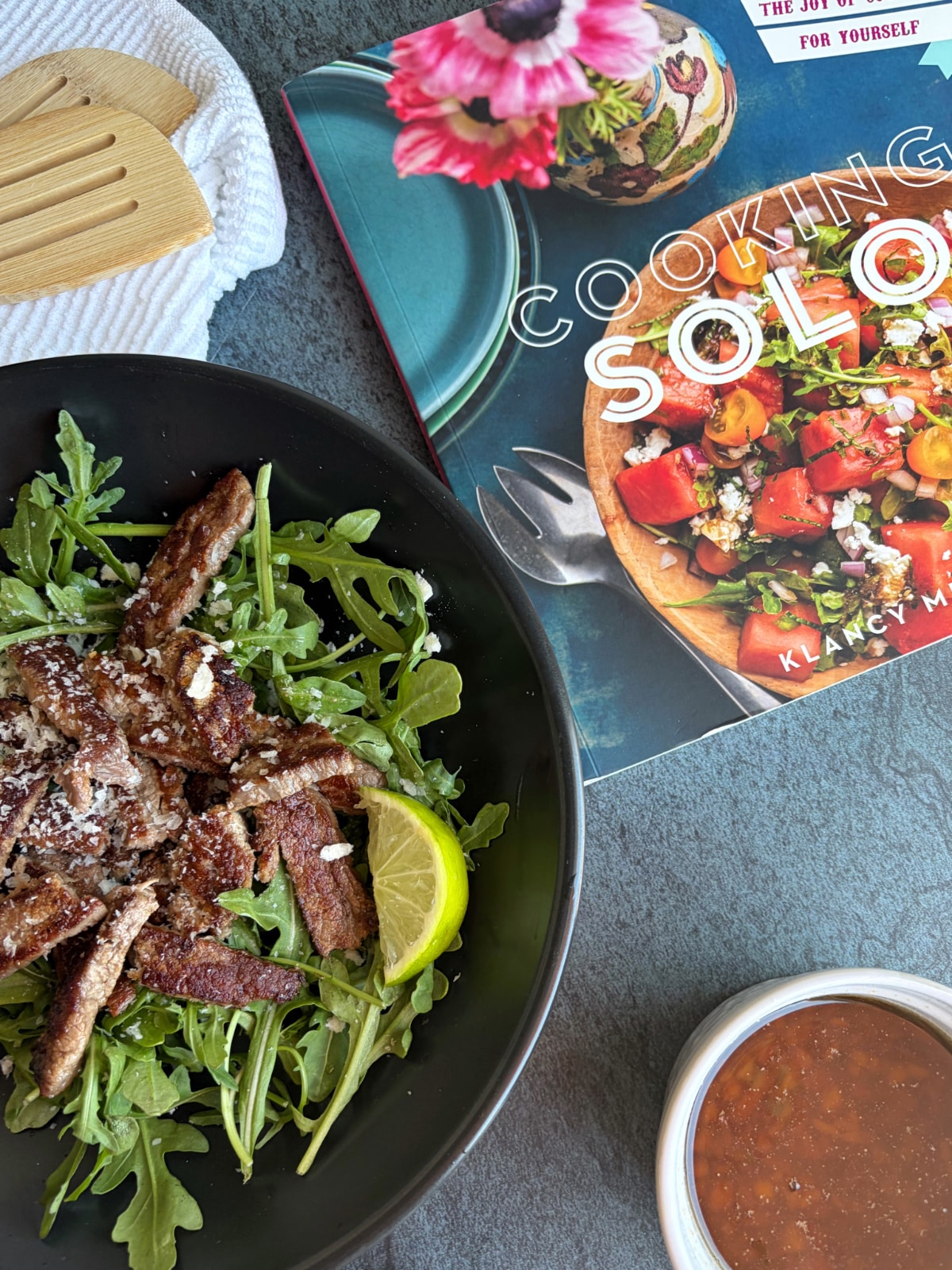 A bowl of soy lime beef stir fry next to a cookbook titled Cooking Solo.