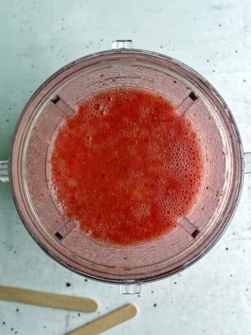 A blender cup filled with blended strawberries, cranberry juice, and honey.