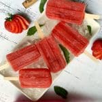 A white tray filled with ice and Strawberry Rose popsicles, with more strawberries on the side.