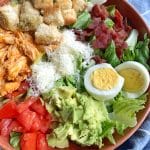 A bowl of Buffalo Chicken Ranch Cobb Salad with a kitchen towel in the background.