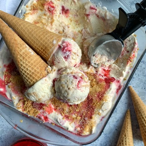 A tray of No-Churn Strawberry Cheesecake Ice Cream with extra cones & strawberry compote on the side.