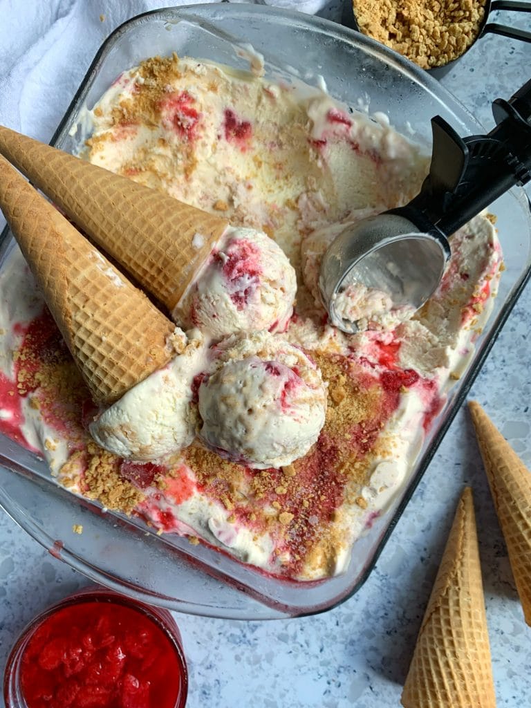 A tray of No-Churn Strawberry Cheesecake Ice Cream with extra cones & strawberry compote on the side.