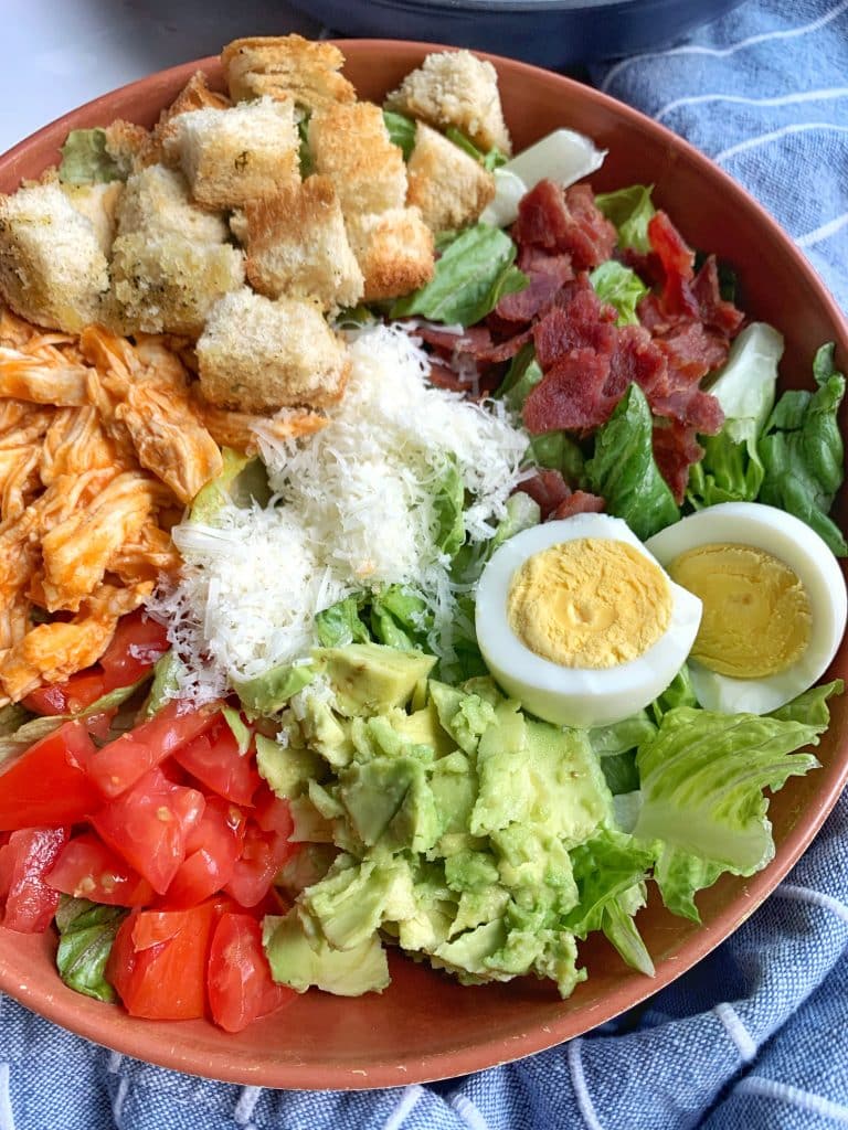 A bowl of Buffalo Chicken Ranch Cobb Salad with a kitchen towel in the background.