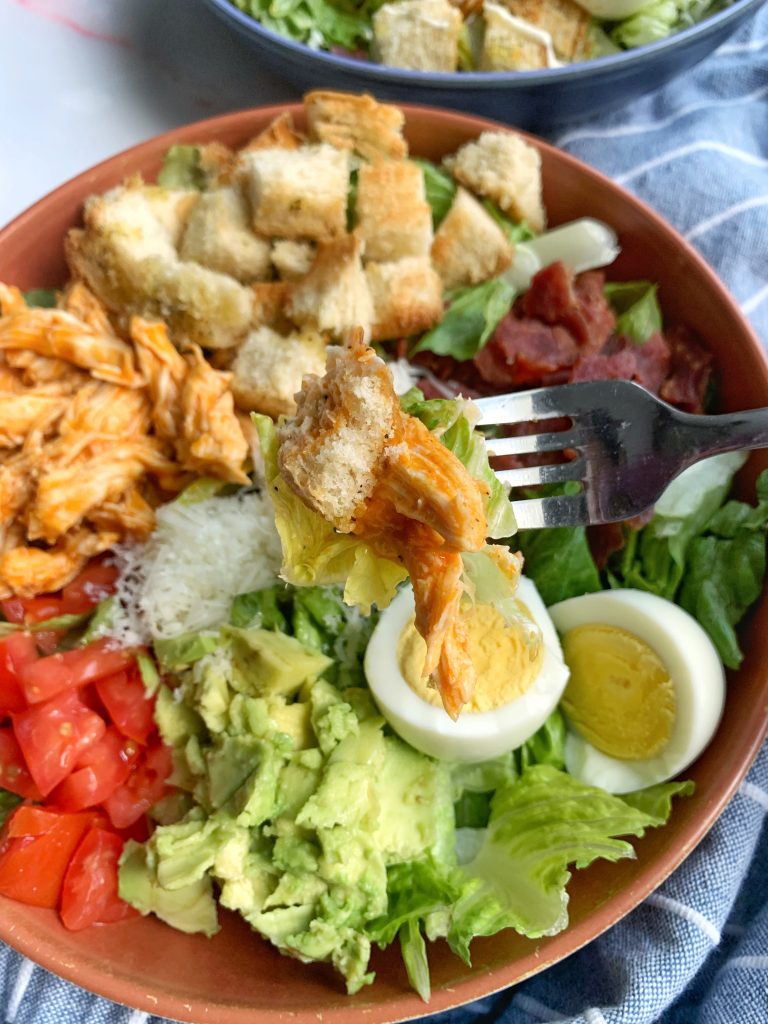 A bowl of Buffalo Chicken Ranch Cobb Salad with a kitchen towel in the background.