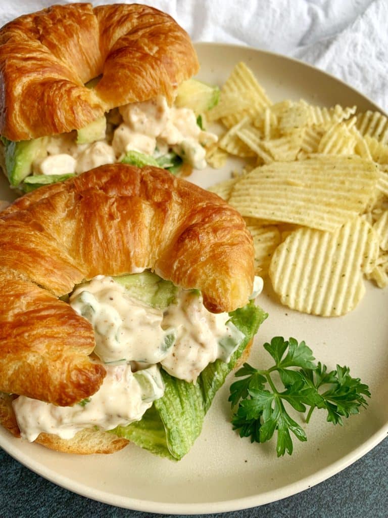 A plate of two cold shrimp salad sandwiches on croissants with chips on the side.