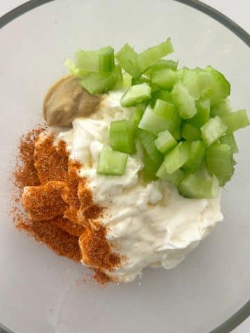 A glass bowl filled with chopped celery, mayonnaise, dijon, and a red spice blend.