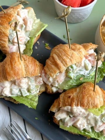 A tray of mini croissant sandwiches filled with shrimp salad.