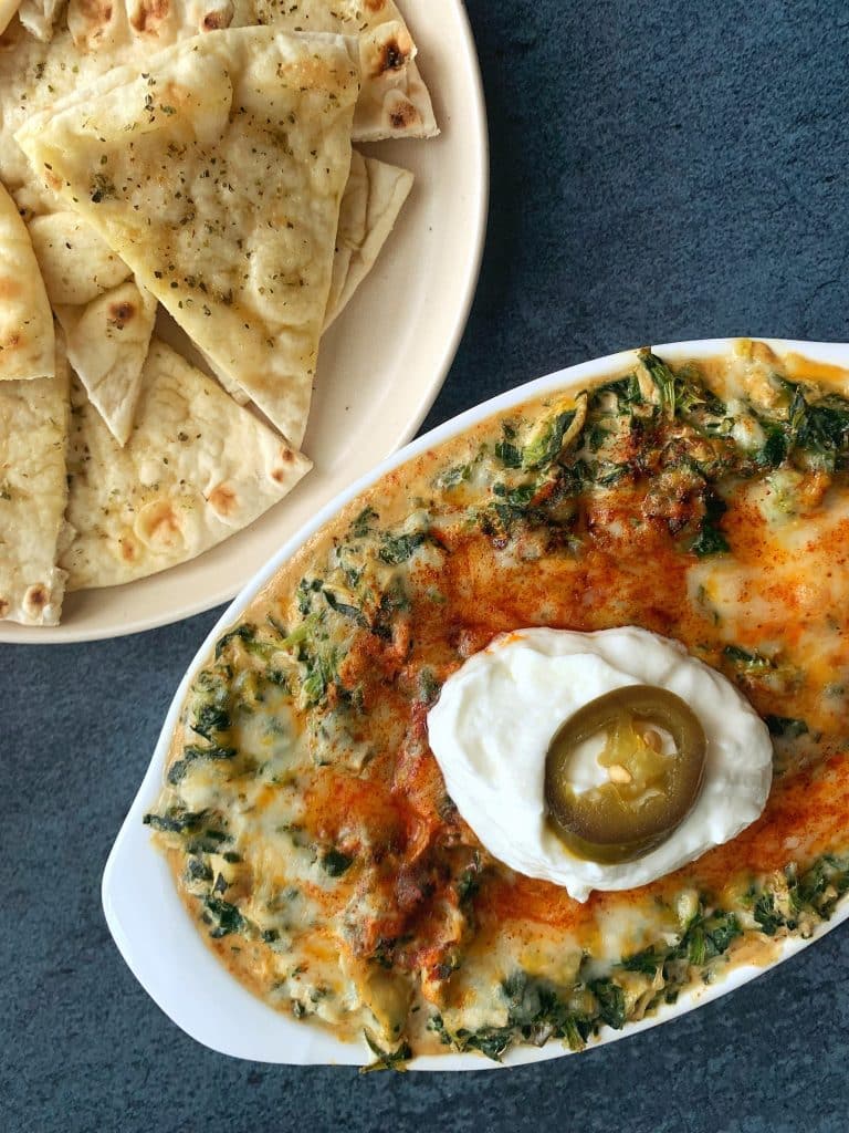 A bowl of Hot Crab Spinach & Artichoke Dip with pita chips on the side.