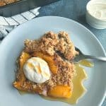 A fork scooping a piece of peach cobbler baked oats with cinnamon cream and syrup on top.
