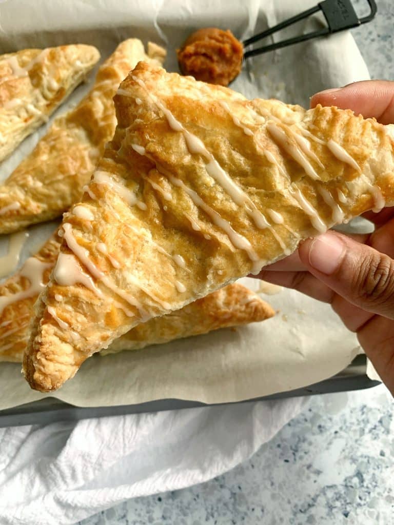A hand holding a Roasted Sweet Potato Turnover with more sweet potato mash in the background.
