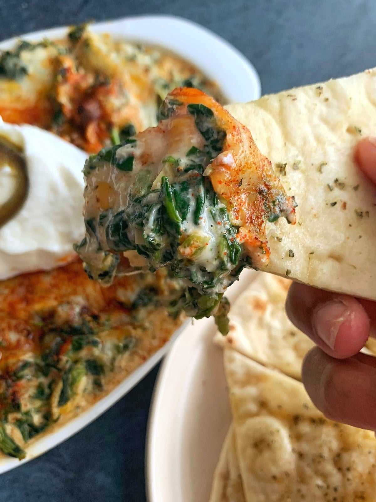 Hot Crab Spinach Dip on the corner of a pita chip being held up over the pan.