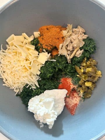 A large bowl filled with the ingredients for crab spinach dip, before mixing together.