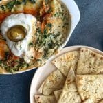 A bowl of Hot Crab Spinach & Artichoke Dip with pita chips on the side.