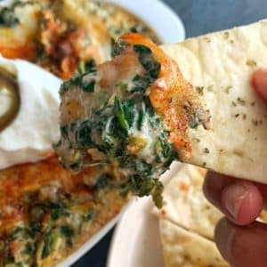 A hand holding up a slice of pita bread with crab spinach dip on top.