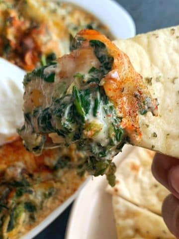 A hand holding up a slice of pita bread with crab spinach dip on top.