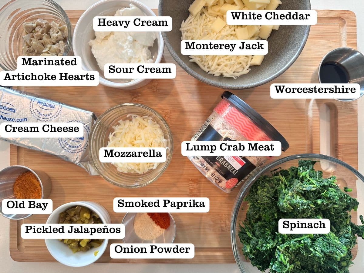 A wooden board filled with ingredients for crab spinach dip, including cream cheese, cheese, and lump crab meat.