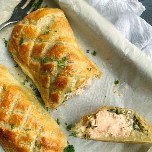 A sheet pan with two Salmon Wellingtons, one with a slice cut out of it.
