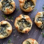 A serving of pesto spinach puffs on a wooden board with grated parmesan.