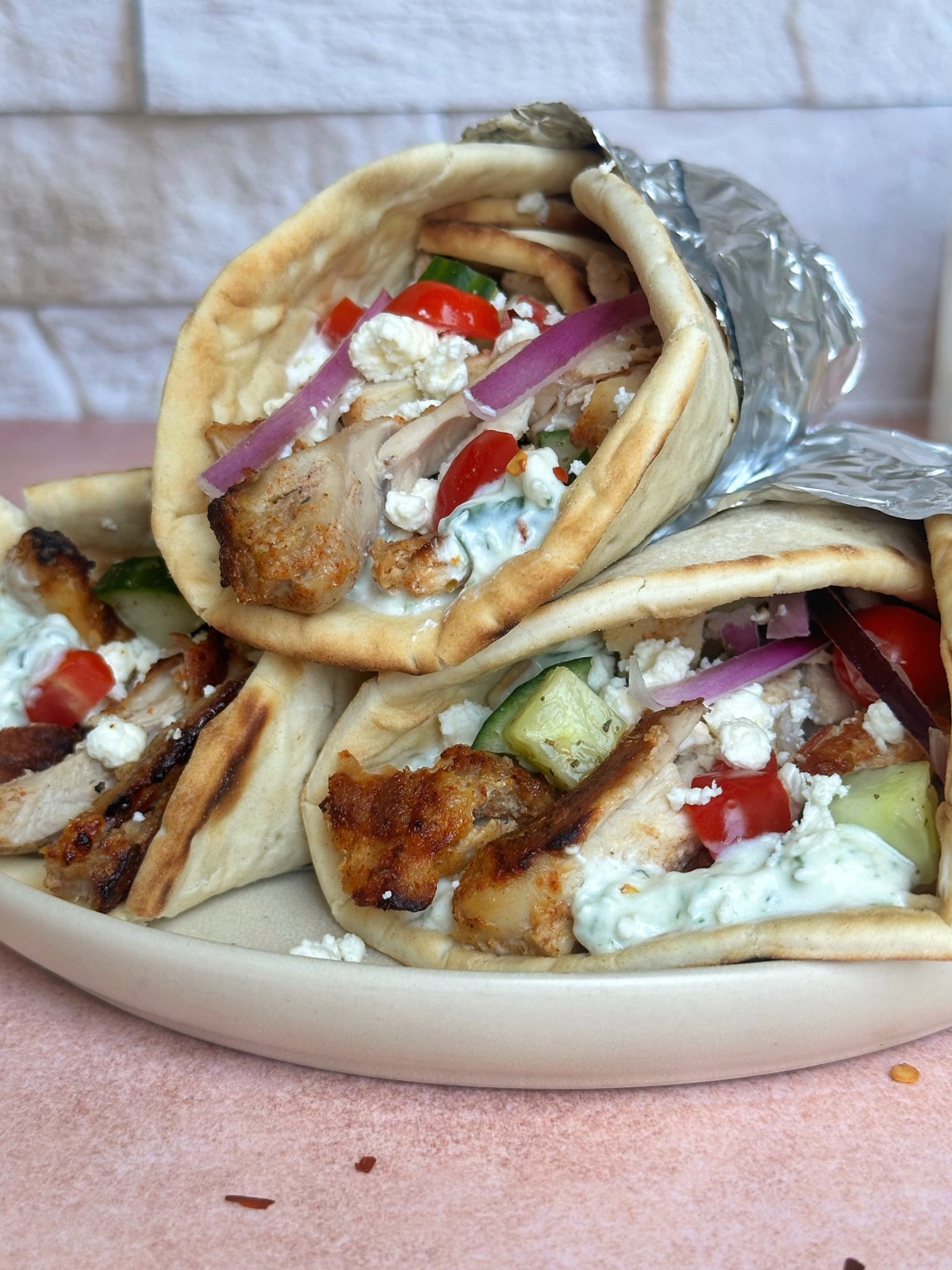 A plate of three chicken gyros wrapped in foil, stacked on top of each other.