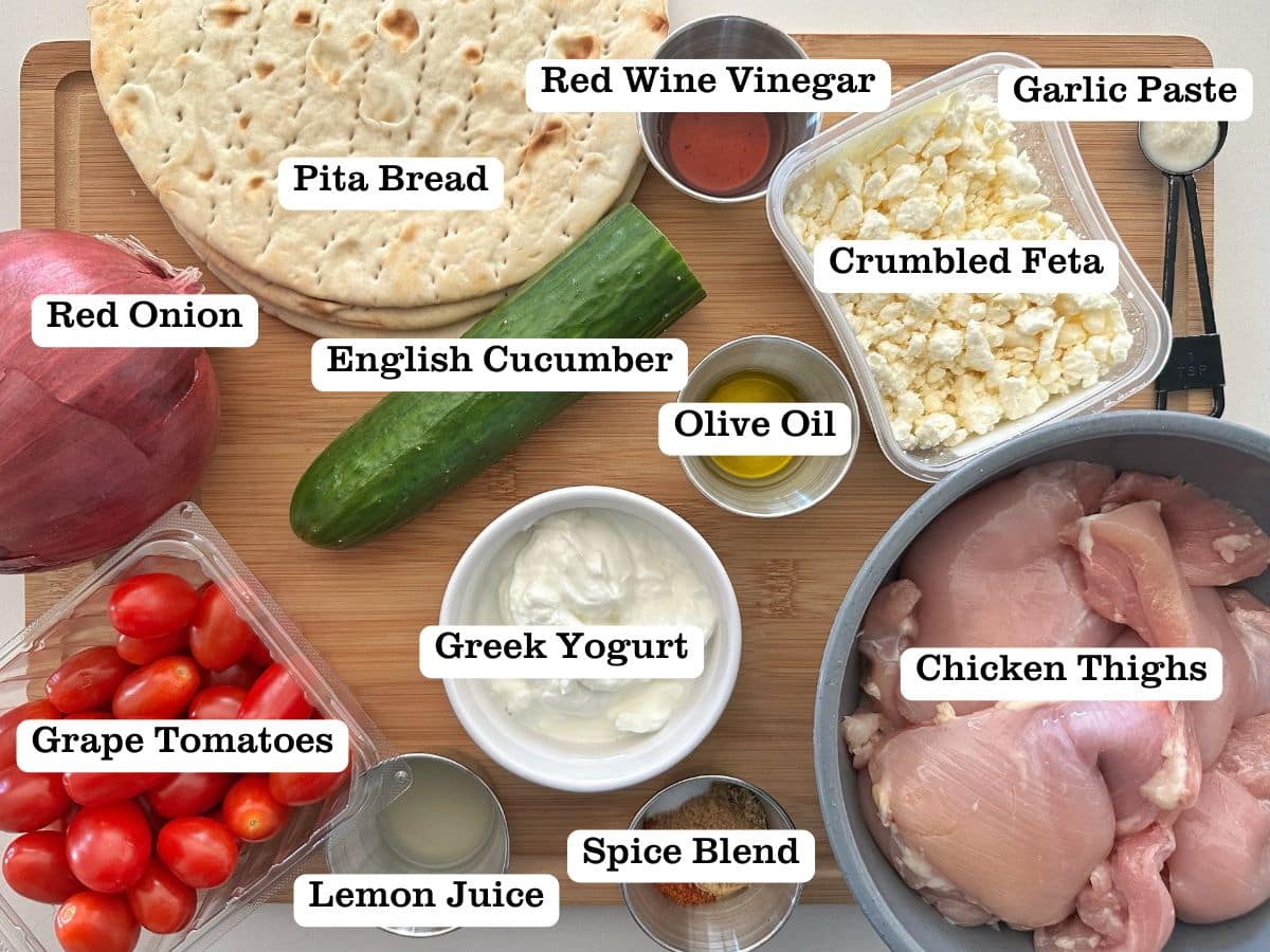 A wooden board containing bowls of ingredients for homemade chicken gyros.