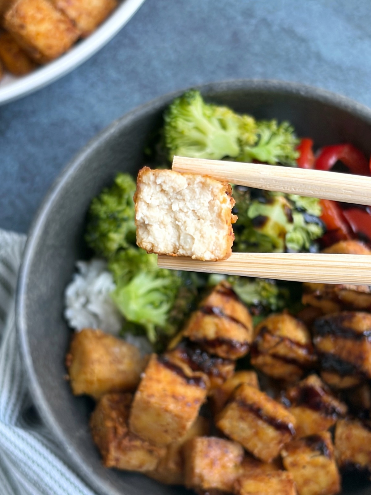A pair of chopsticks holding up a piece of crispy tofu cut in half to see the interior texture.